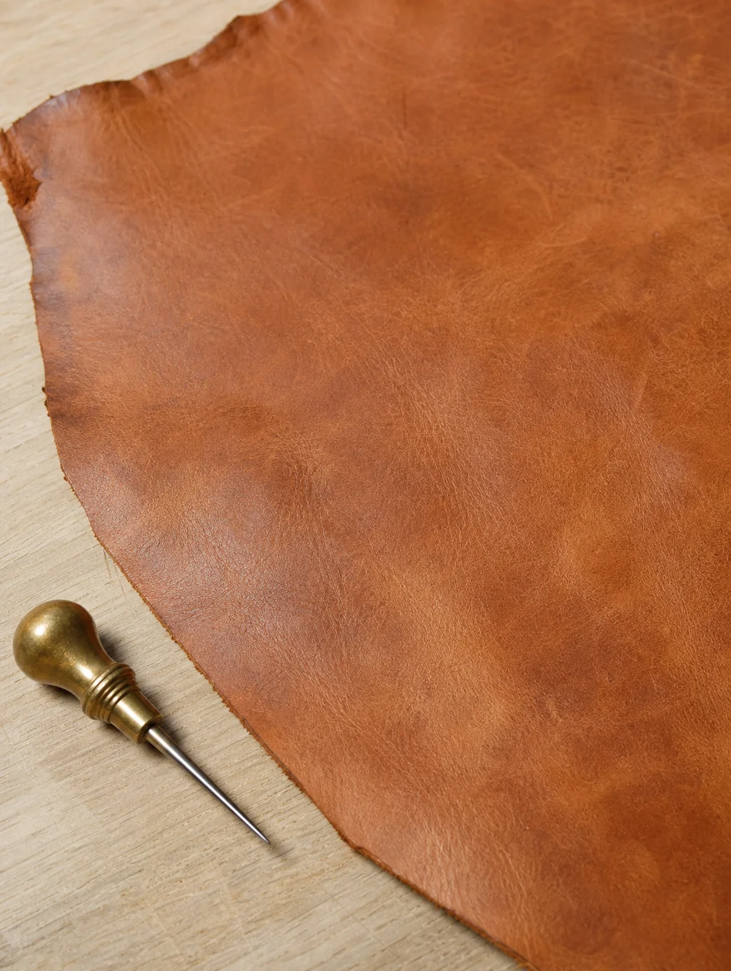 Close up of vegetable-tanned leather grain and workshop edge beveling tools in natural morning sunlight